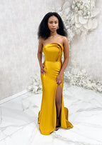 Bridesmaid wearing a modern strapless fitted bridesmaid dress with stretch. The dress has a slit at the leg, and curved architectural detailing at the neck, and is shown in a golden vibrant yellow on a black model.