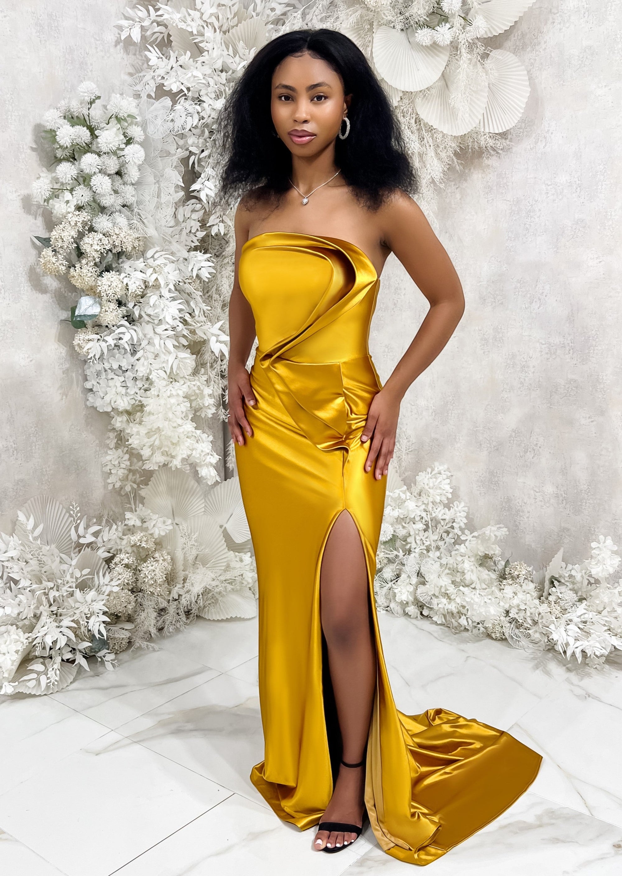Bridesmaid wearing a modern strapless fitted bridesmaids dress with stretch. Dress has a slit at the leg, curved architectural detailing, and is shown in a golden vibrant yellow on a black model. plus size bridesmaid dress