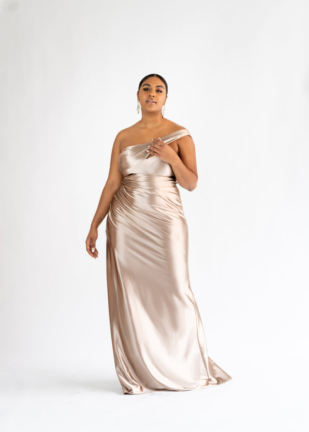 Aura champagne stretch satin one-shoulder bridesmaid dress with a draped bodice, shown on a curvy model