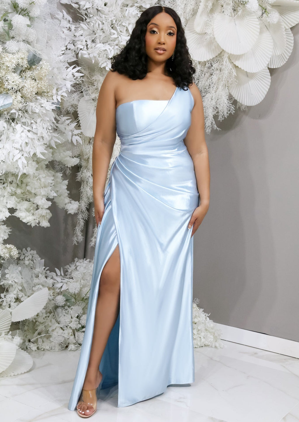 Curvy mid-size bridesmaid wearing a one-shoulder column bridesmaid dress with stretch. This dress has a slit at the leg and ruching throughout to flatter all body types and is shown on a black model.