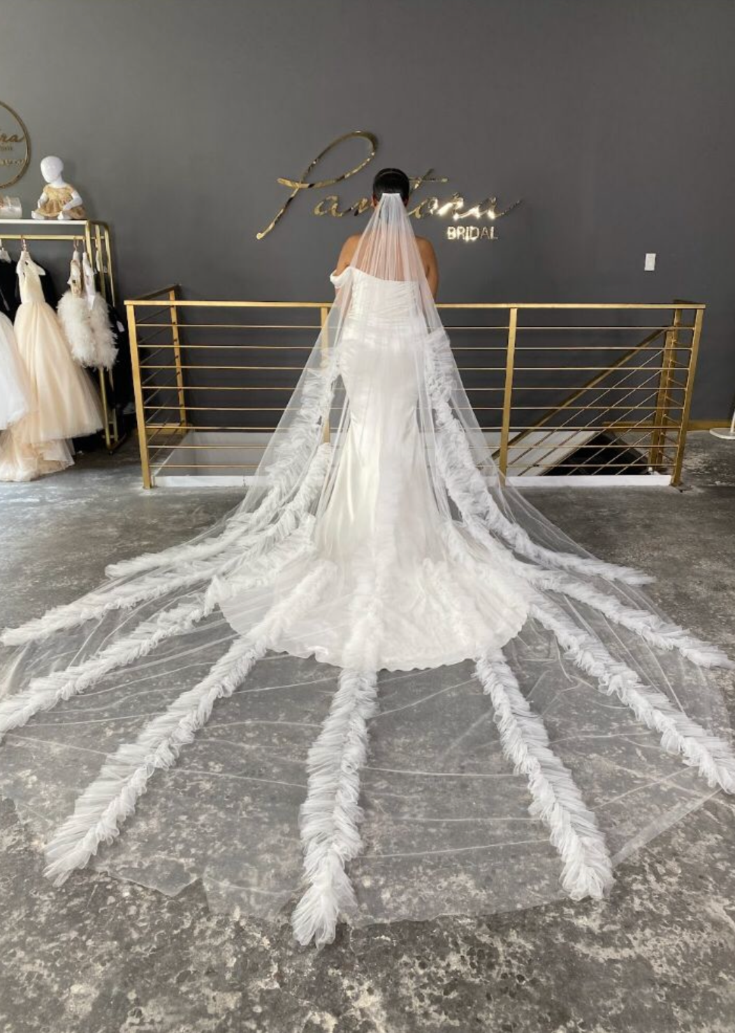 Beautiful cathedral length wedding veil for bride shown in a bridal store. Tulle veil features beautiful ruffle detailing that cascades down the veil for a dramatic finish. 