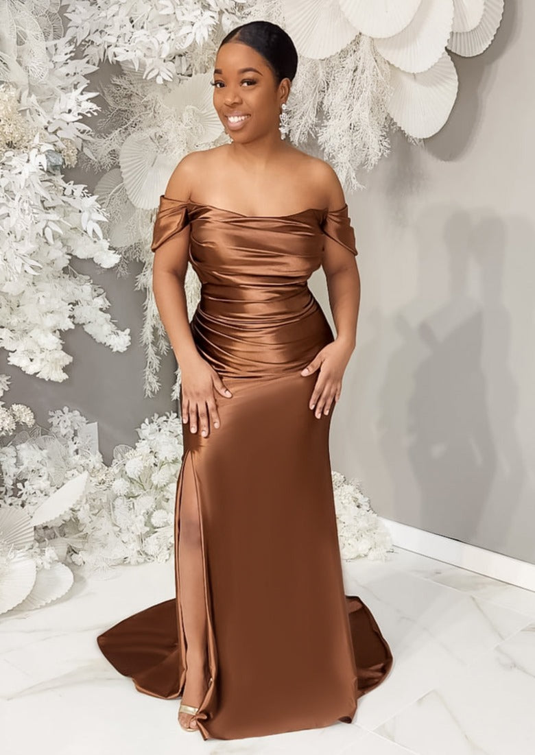 Petite black model wearing a fitted stretch satin bridesmaid dress with off-the-shoulder detailing, ruching, and slit on curvy model