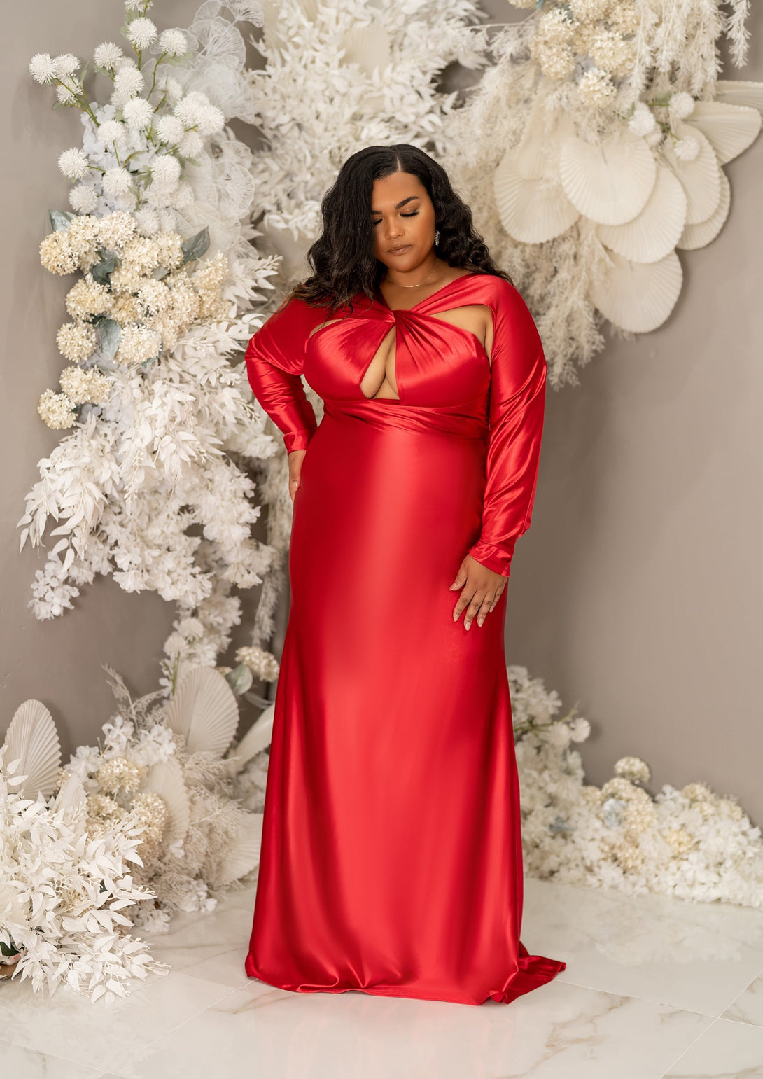 Plus size curvy bridesmaid wearing a long sleeve fitted bridesmaid dress with twisted open halter neckline. Shown on a plus size curvy black model in a vibrant red.