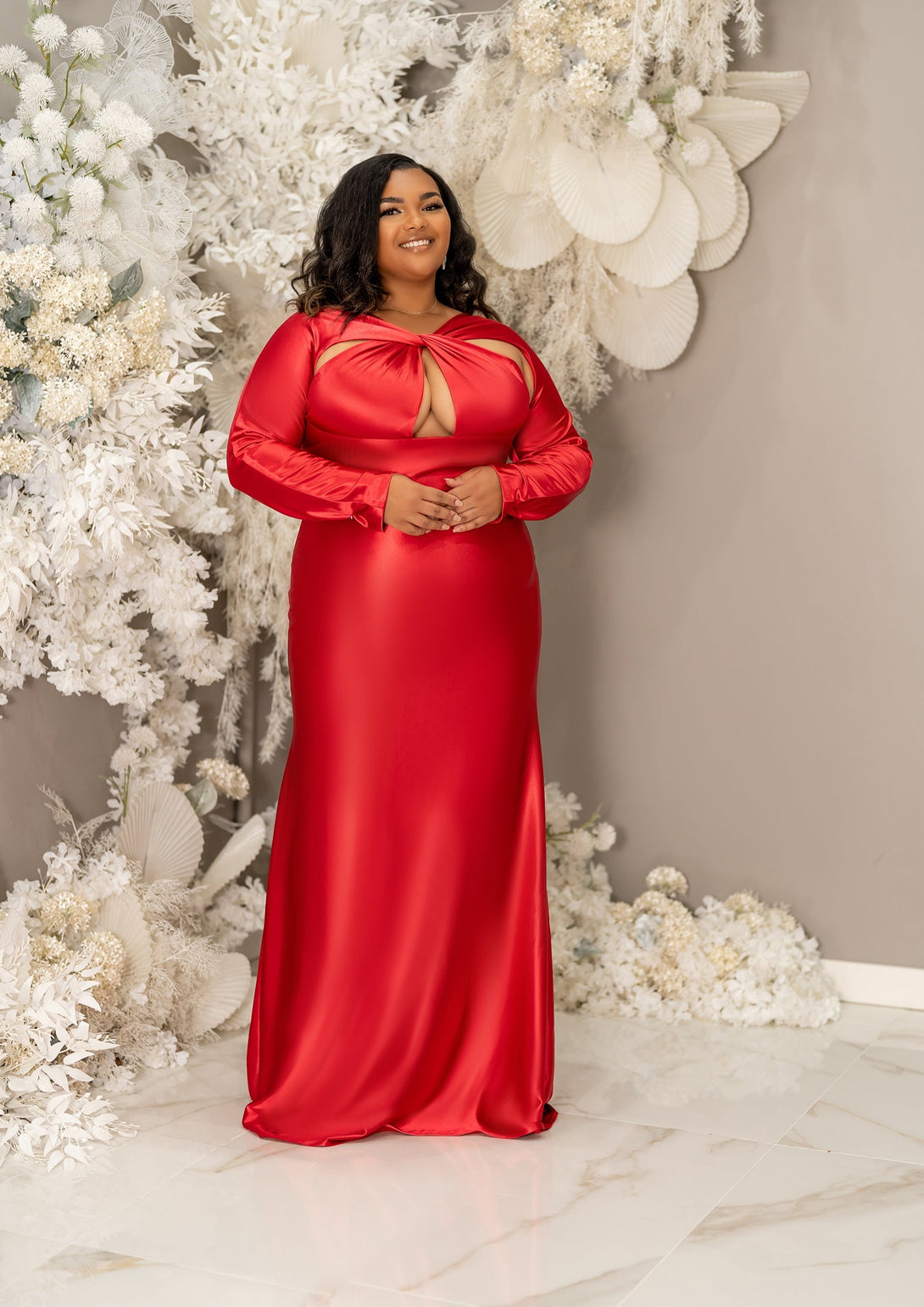 Plus size curvy bridesmaid wearing a long sleeve fitted bridesmaid dress with twisted open halter neckline. Shown on a plus size curvy black model in a vibrant red.