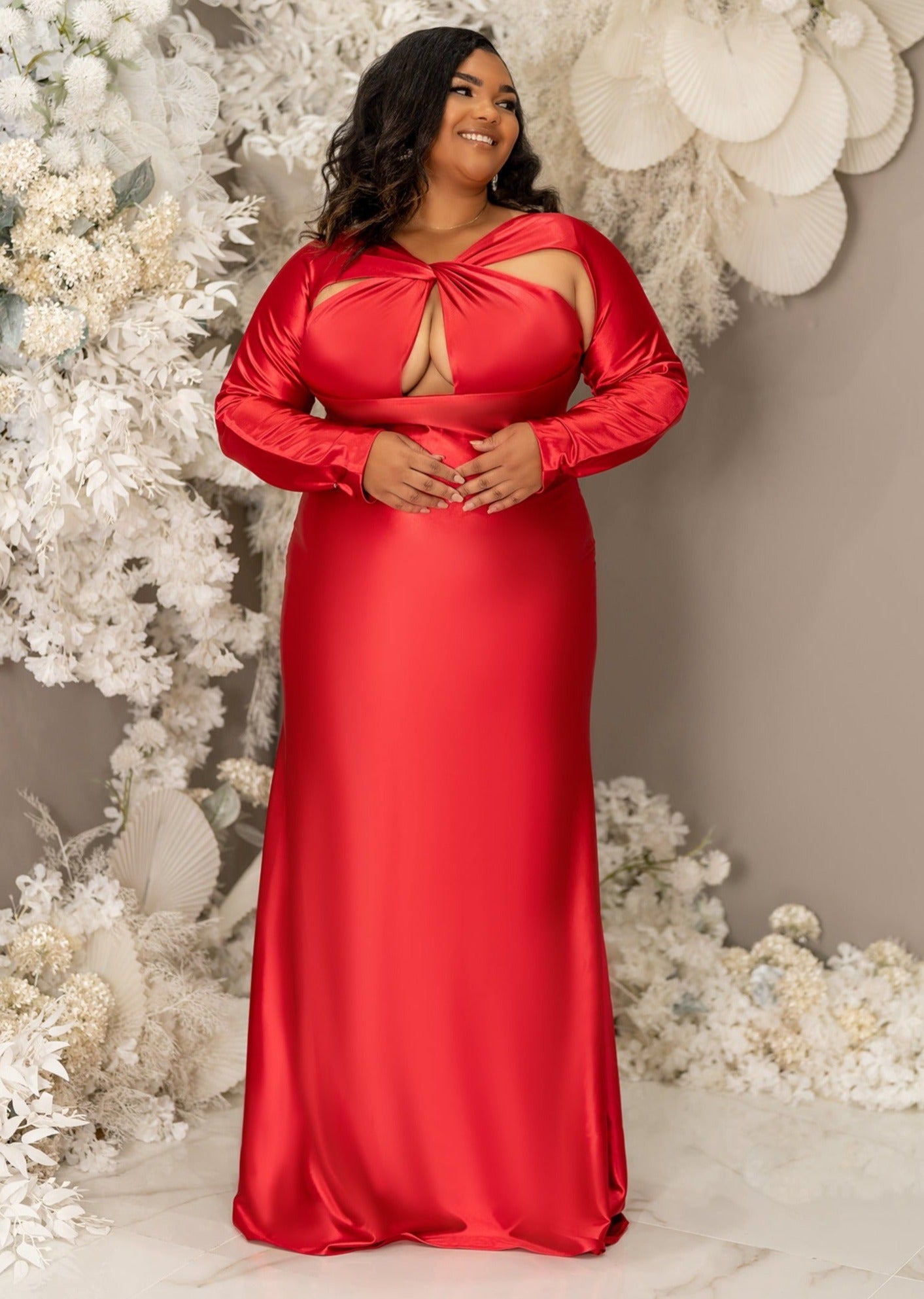 Plus size curvy bridesmaid wearing a long sleeve fitted bridesmaid dress with twisted open halter neckline. Shown on a plus size curvy black model in a vibrant red. curvy black model in a vibrant red.