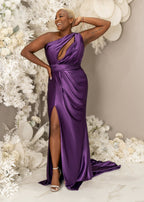 Plus size curvy bridesmaid wearing fitted stretch satin bridesmaid dress in purple, dress has one shoulder detailing, ruching, keyhole neckline, and slit.