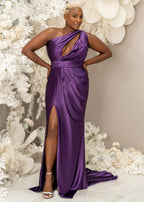 Plus size curvy bridesmaid wearing fitted stretch satin bridesmaid dress in purple, dress has one shoulder detailing, ruching, keyhole neckline, and slit.