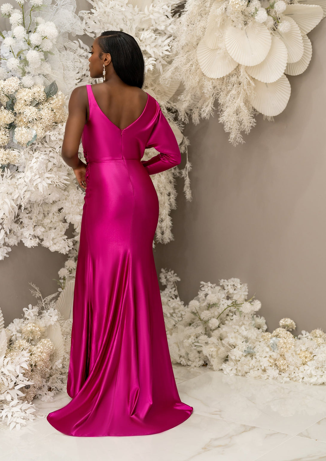 Jewel tone pink fitted V-Neck bridesmaid dress with an asymmetrical Dolman sleeve, has gathering and gentle draping. Shown on a petite black model, this style features a leg slit and is made in stretch satin to flaunt curves - alternative back view