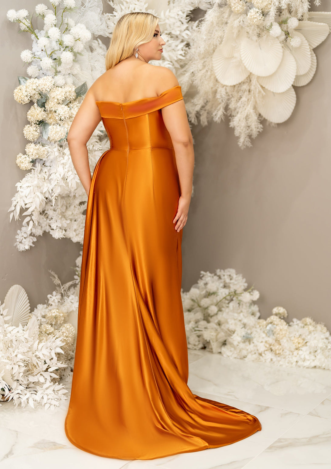 Plus size bridesmaid in asymmetrical fitted stretch satin bridesmaid dress with ruching at the waist and through the skirt and an off-the-shoulder strap. This style is designed to flatter and complement all body types. Shown in burnt orange on a curvy model. - alternative back view