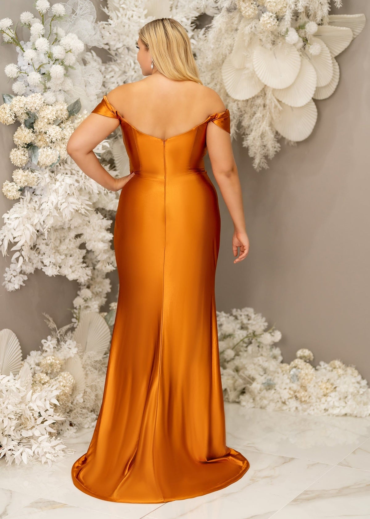 Fitted burnt orange stretch satin bridesmaid dress with off the shoulder detailing, ruching, and slit on plus size model - back view