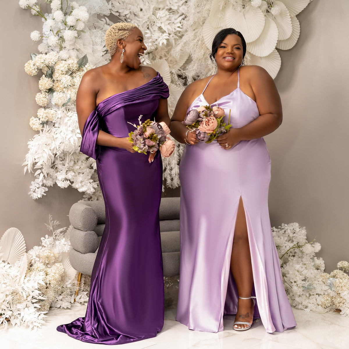 Plus-size and mid-size bridesmaids in shades of purple in stretch satin bridesmaid dresses holding bouquets and celebrating the shape of their bodies.
