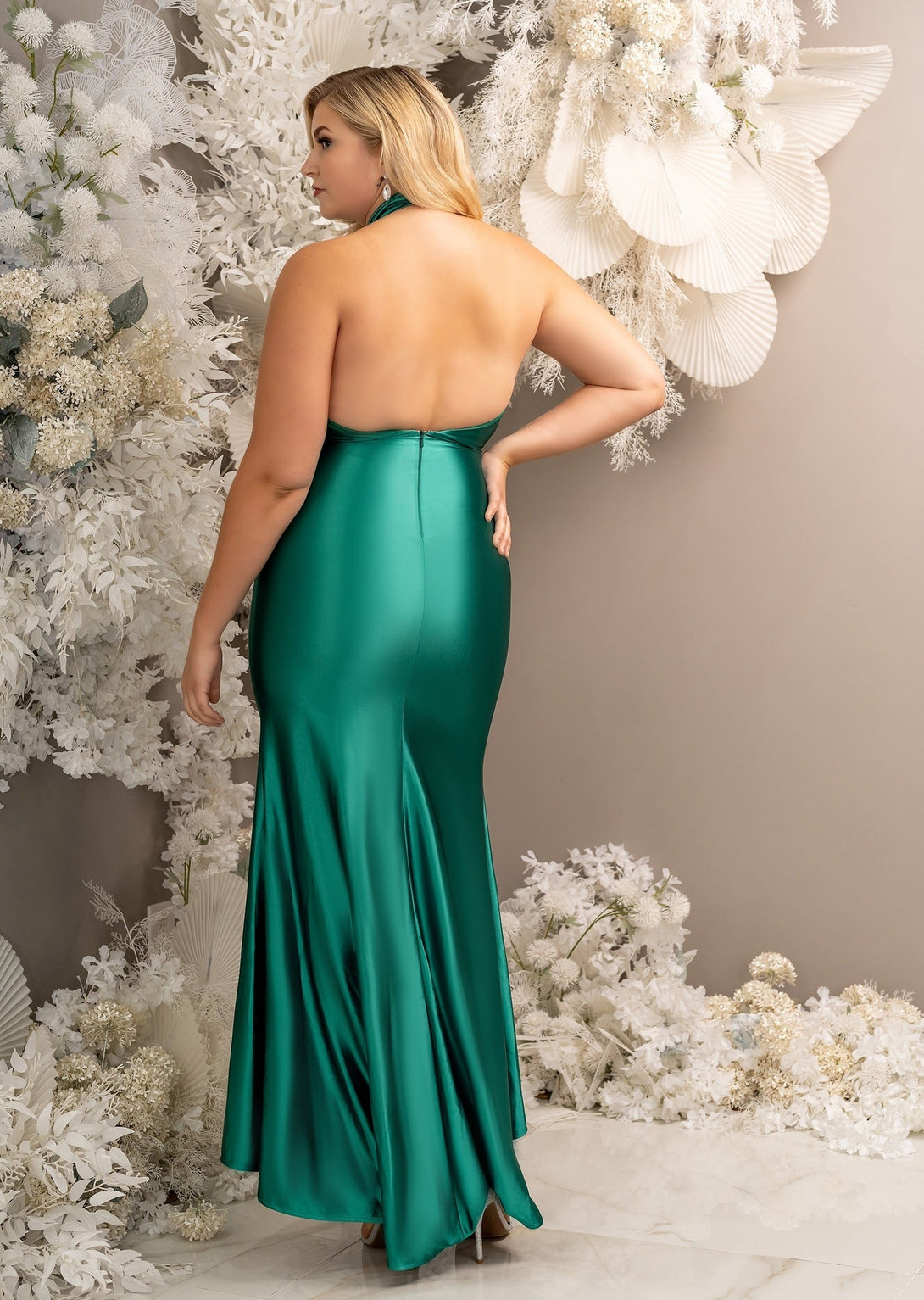 Bridesmaid wearing a classic fitted bridesmaid dress with open back and twisted halter neckline. Shown in emerald green on a plus size model - back view